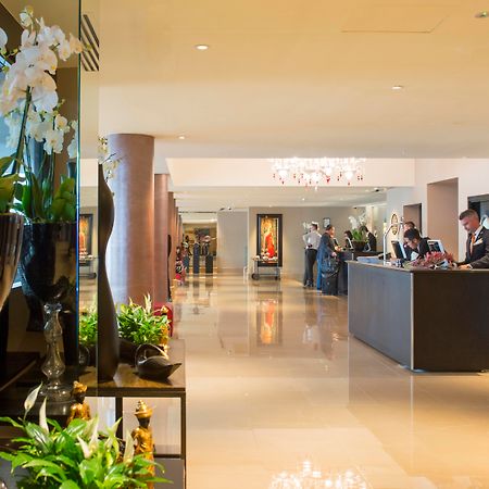 The May Fair, A Radisson Collection Hotel, Mayfair Londýn Exteriér fotografie The photo shows a spacious and elegantly designed hotel lobby. There are decorative elements such as flowers and plants along the sides, enhancing the luxurious atmosphere. In the background, you can see the reception area with staff members engaged 