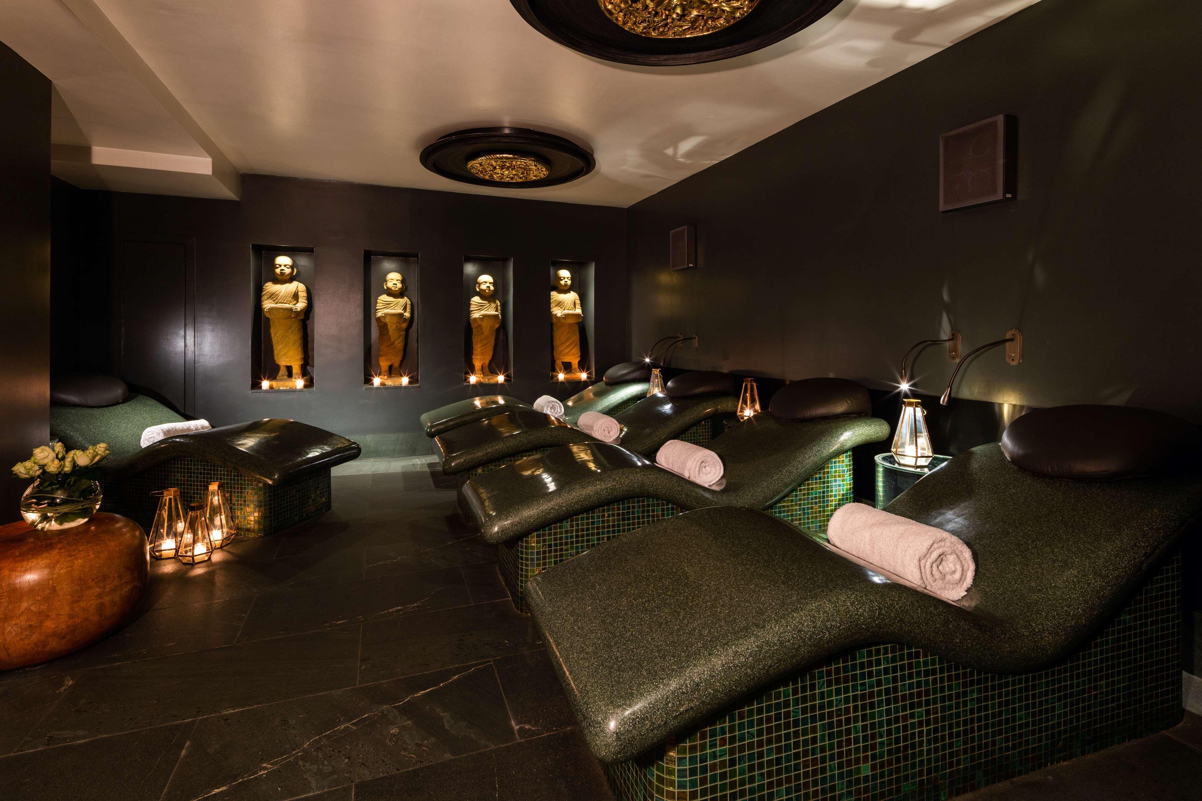 The May Fair, A Radisson Collection Hotel, Mayfair Londýn Exteriér fotografie The photo shows a tranquil spa environment. It features lounge chairs with curved backs, designed for relaxation, positioned in a dimly lit room. The walls are decorated in dark tones, providing a calming atmosphere. There are illuminated statues or 