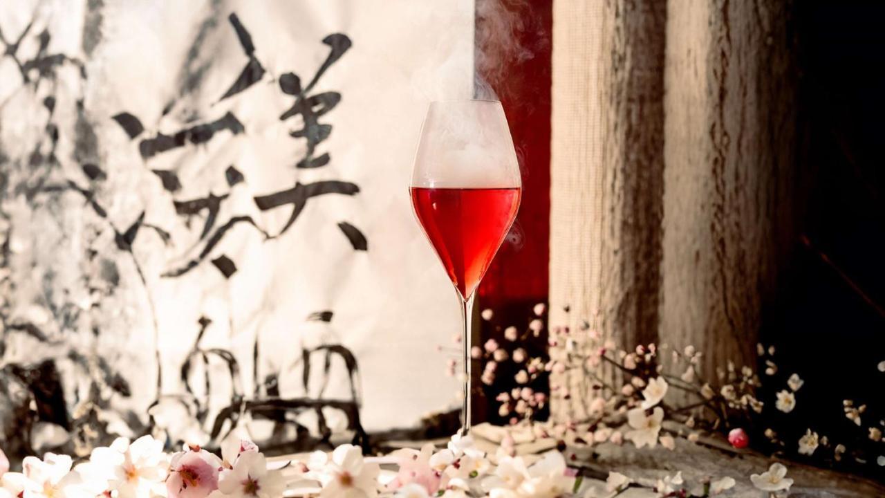 The May Fair, A Radisson Collection Hotel, Mayfair Londýn Exteriér fotografie The photo features a glass of red beverage, elegantly presented in a stemmed glass. The drink emits a mist, adding an ethereal quality to the image. Surrounding the glass are delicate pink flowers, enhancing the aesthetic appeal. In the background, t