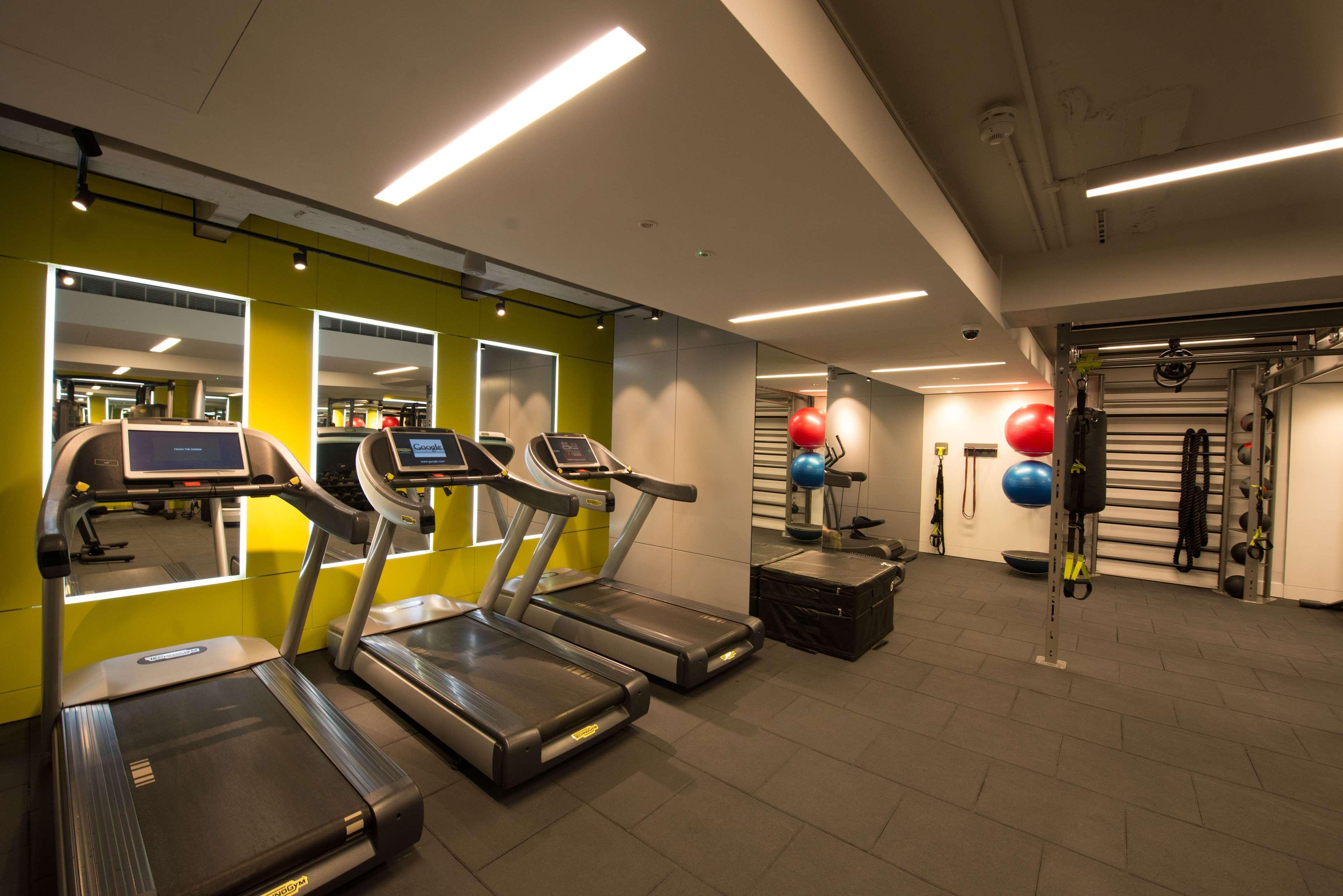 The May Fair, A Radisson Collection Hotel, Mayfair Londýn Exteriér fotografie The photo shows a modern gym interior featuring several exercise equipment. In the foreground, there are three treadmills aligned along a wall with mirrors. The wall behind the treadmills is painted a vibrant green, enhancing the energetic atmosphere