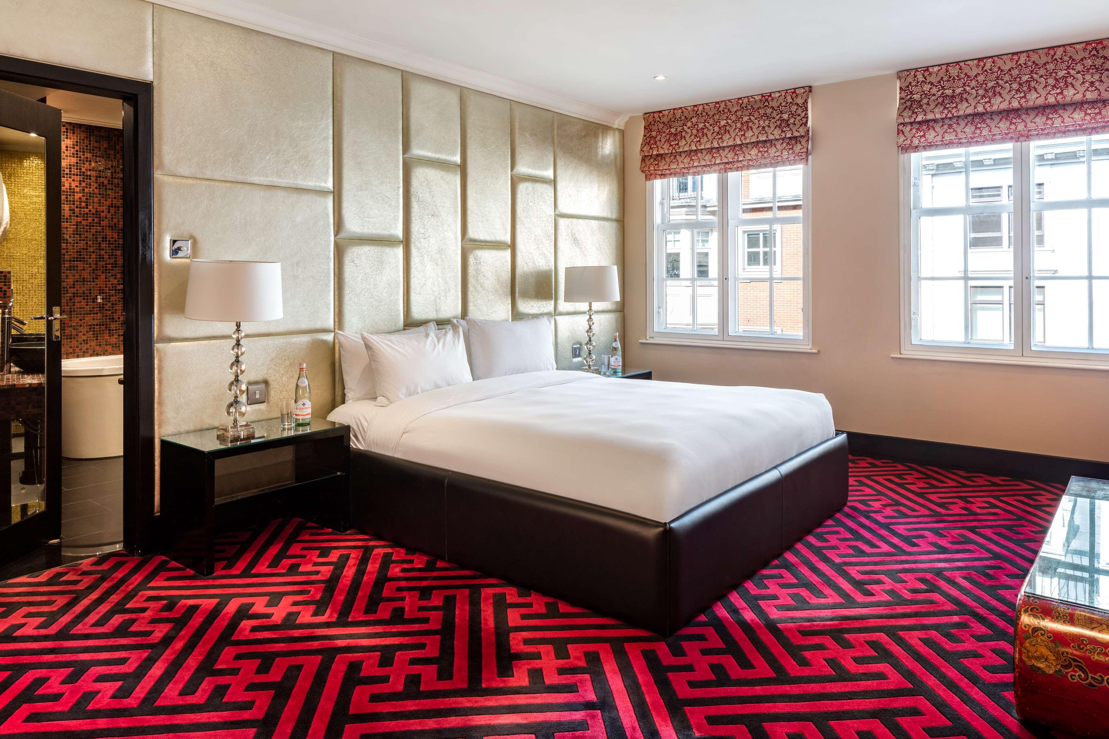 The May Fair, A Radisson Collection Hotel, Mayfair Londýn Exteriér fotografie The photo shows a modern hotel room featuring a large bed with white bedding. The walls are accented with a stylish, textured design, and the room is illuminated by natural light coming from two windows, which have patterned blinds. The floor is cove