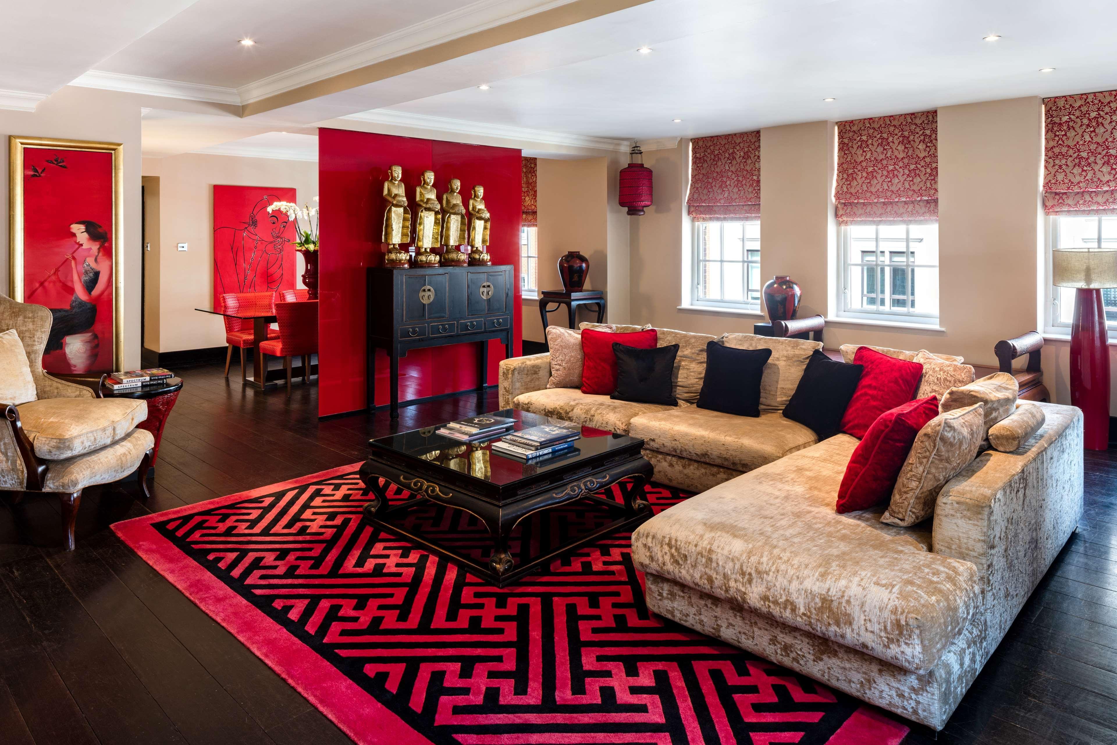 The May Fair, A Radisson Collection Hotel, Mayfair Londýn Exteriér fotografie The photo shows a stylish and elegant living room designed with a modern aesthetic. The space features a large, plush sofa in a light color, complemented by red and black throw pillows. A dark coffee table sits in the center, adorned with books and d