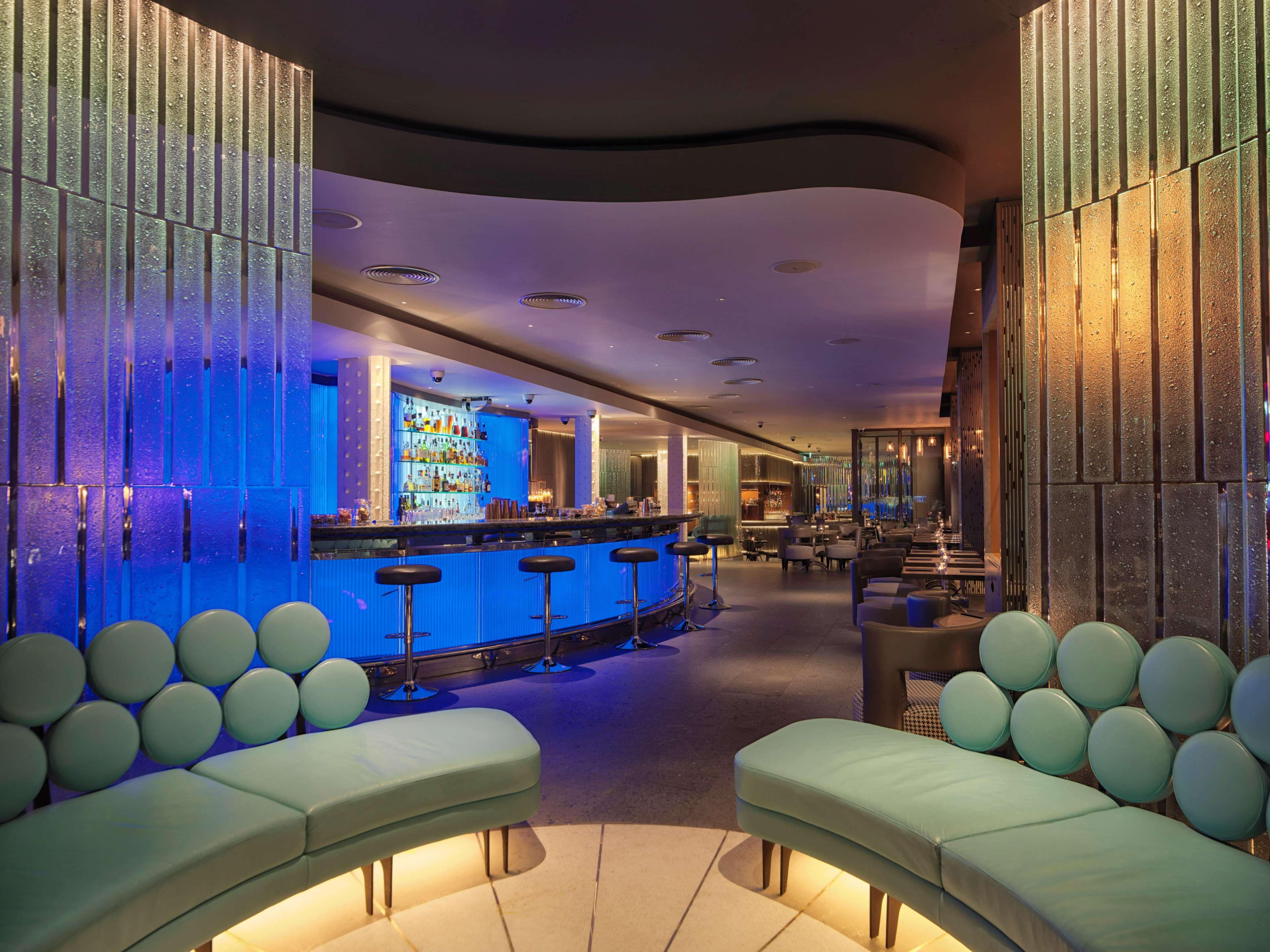 The May Fair, A Radisson Collection Hotel, Mayfair Londýn Exteriér fotografie The photo shows a modern bar or lounge area with a stylish and contemporary design. The interior features curved seating with light green upholstery, creating a relaxed atmosphere. Behind the seating, there is a bar area illuminated with blue lightin