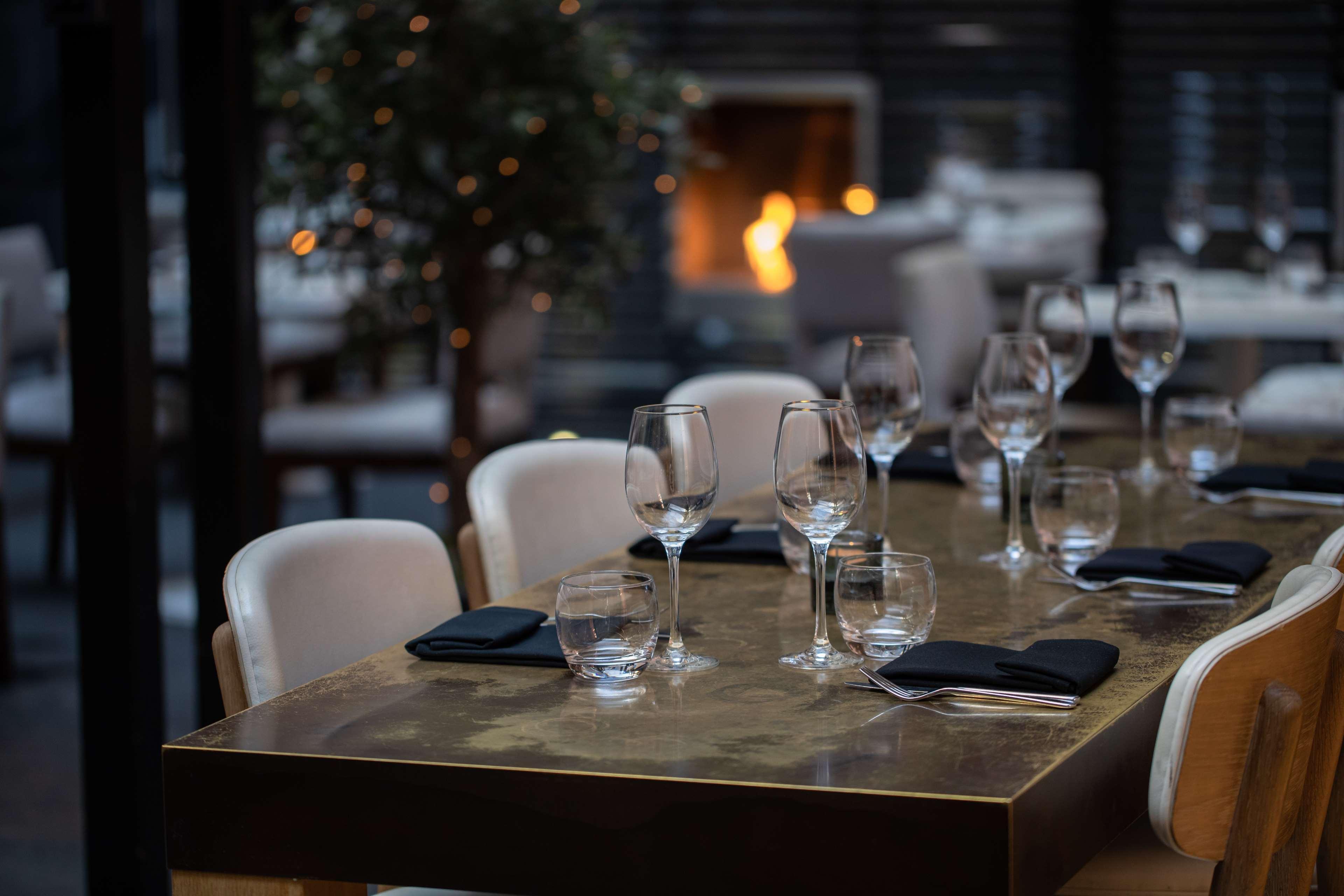 The May Fair, A Radisson Collection Hotel, Mayfair Londýn Exteriér fotografie The photo shows a stylish restaurant dining area. A beautifully set table is in the foreground, featuring elegant glassware and black napkins. The table has a glossy surface and appears to be well-prepared for dining. In the background, there is a co