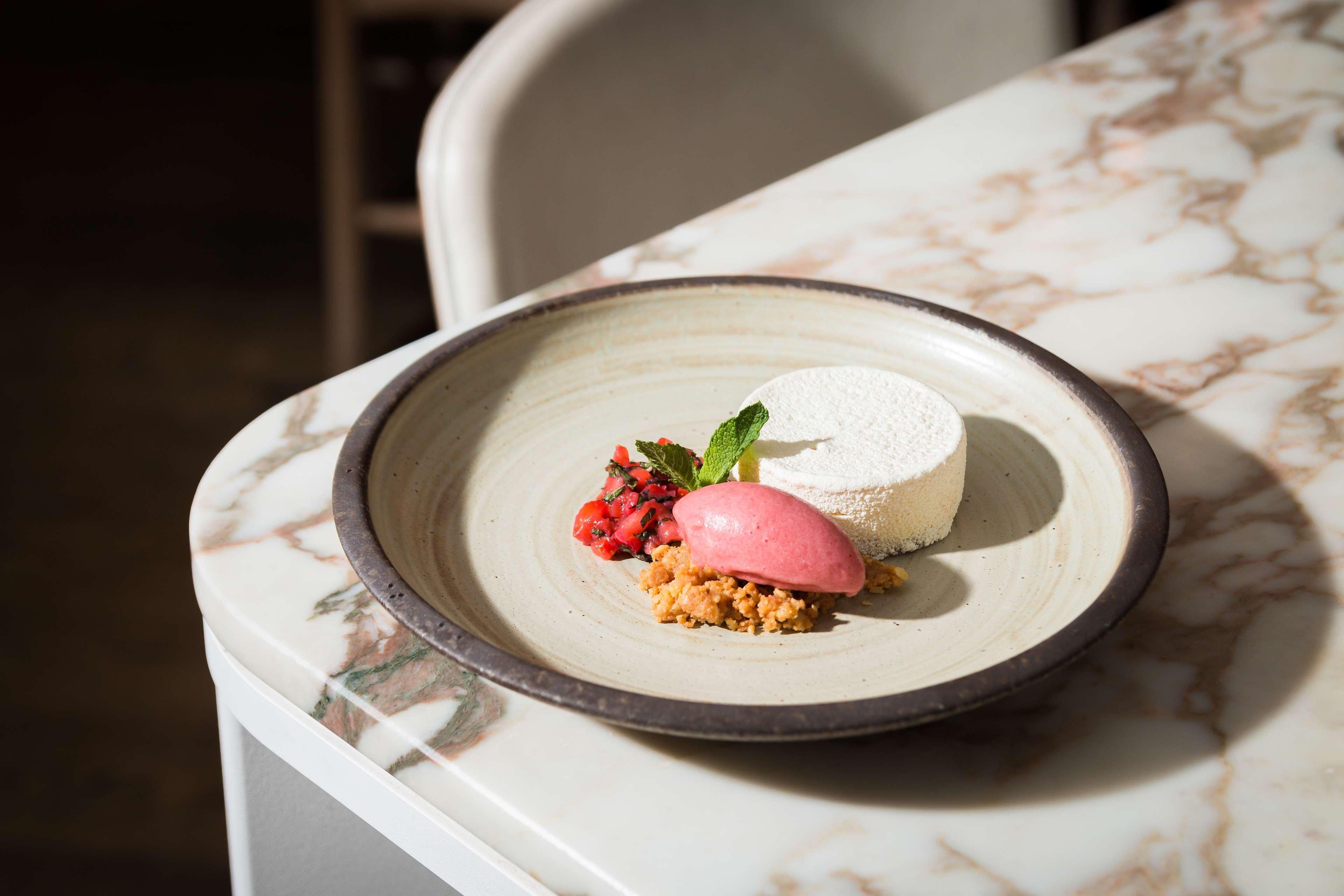 The May Fair, A Radisson Collection Hotel, Mayfair Londýn Exteriér fotografie The photo showcases a beautifully plated dessert on a round, light-colored plate. The dessert features a cylindrical piece of creamy white mousse or panna cotta, accompanied by a vibrant pink scoop of sorbet. There is also a small portion of crumbled