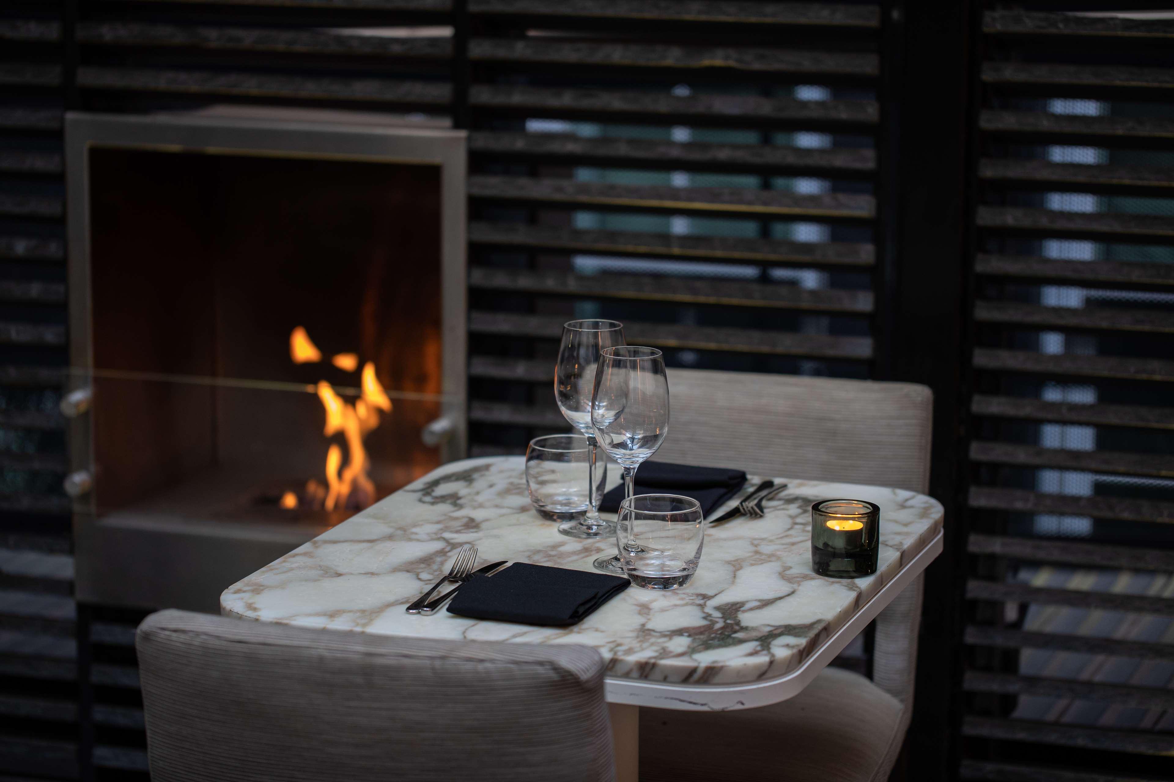 The May Fair, A Radisson Collection Hotel, Mayfair Londýn Exteriér fotografie The photo shows an elegantly set table in a restaurant or cozy dining space. The table has a marble top and is arranged with two wine glasses, water glasses, and dark napkins. There are utensils placed on either side. A small candle sits on the table