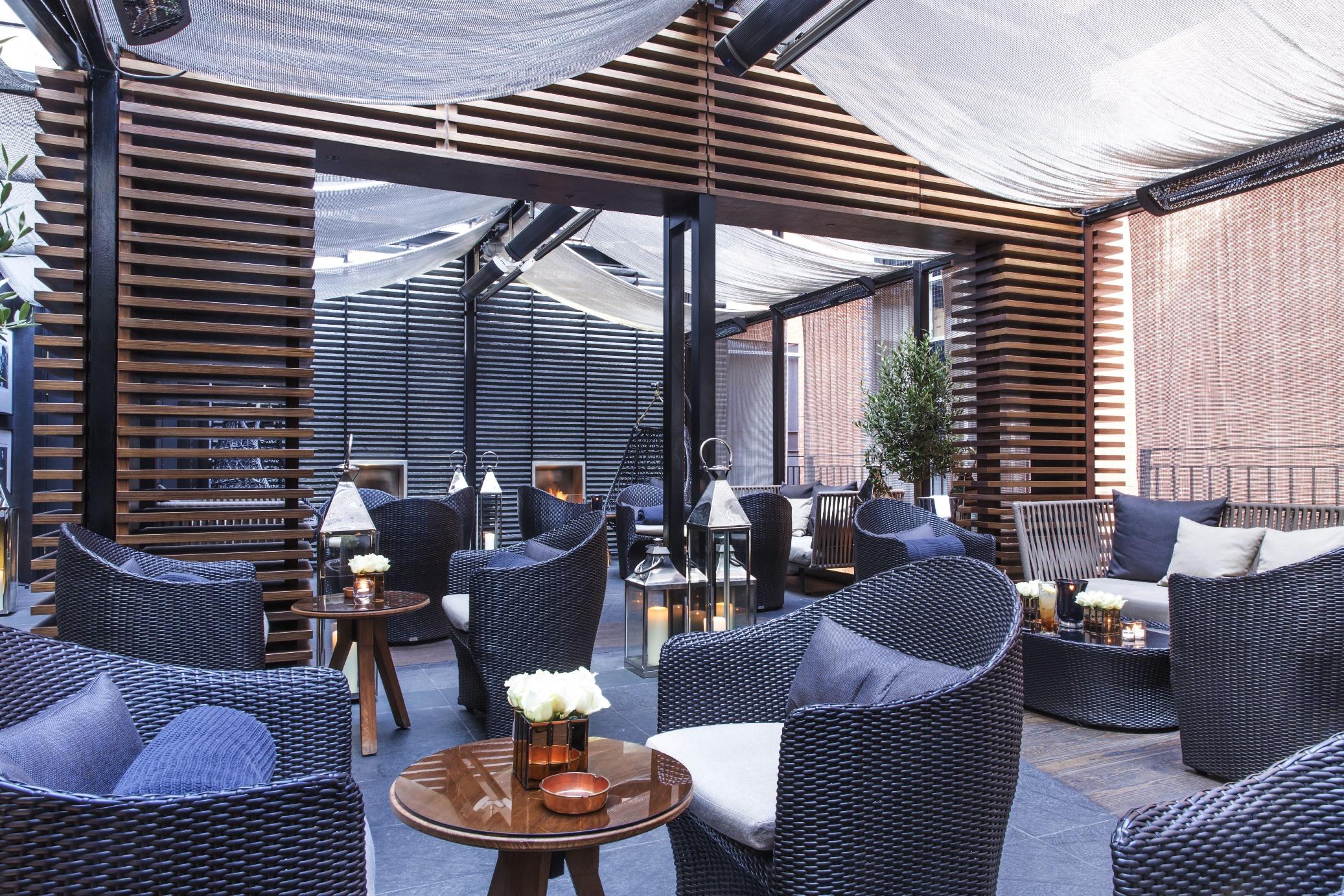 The May Fair, A Radisson Collection Hotel, Mayfair Londýn Exteriér fotografie The photo showcases a stylish indoor lounge area with modern decor. It features a series of comfortable wicker armchairs arranged around wooden tables. The space is adorned with elegant touches like small vases containing flowers on the tables. The c