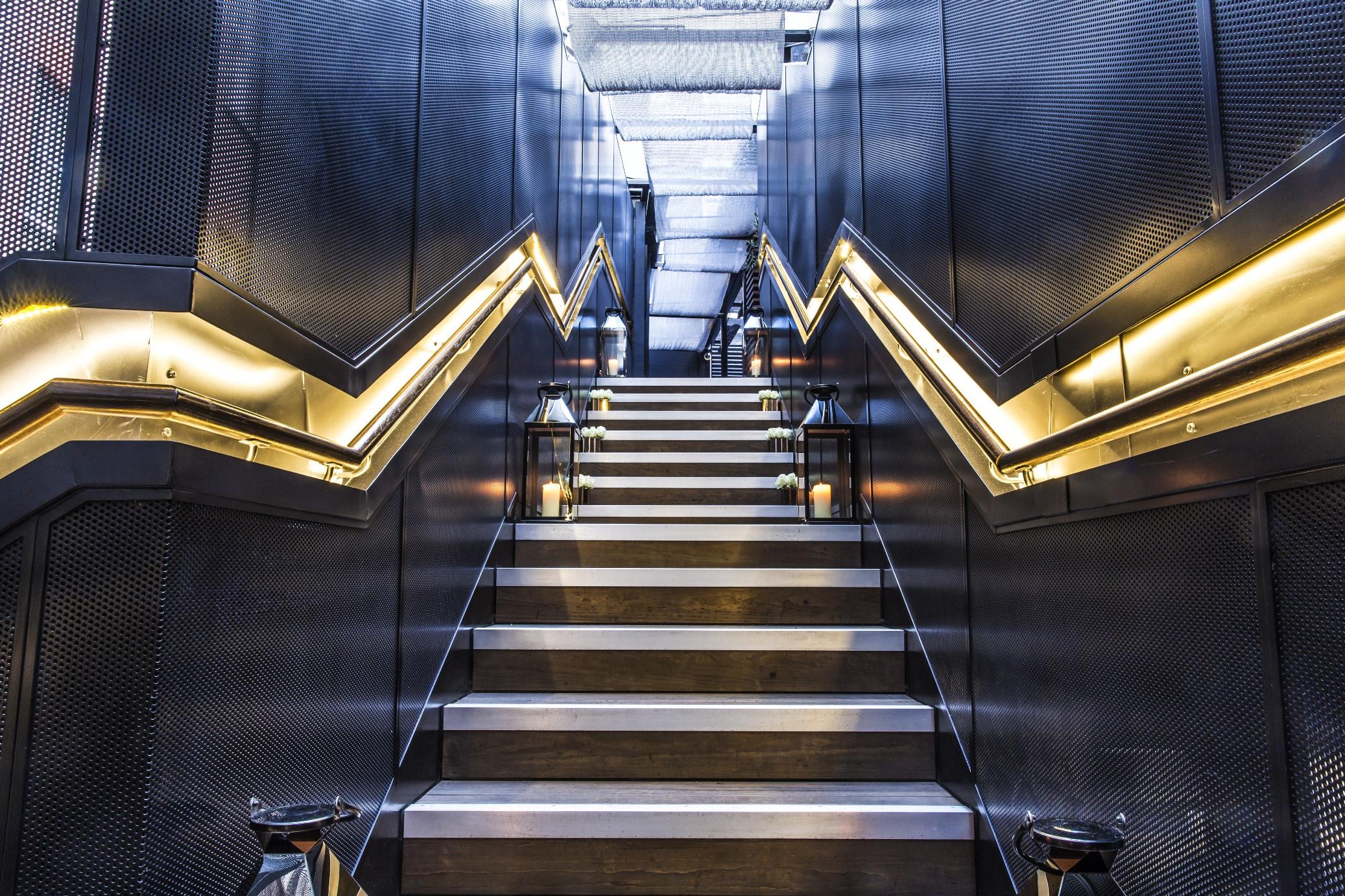 The May Fair, A Radisson Collection Hotel, Mayfair Londýn Exteriér fotografie The photo depicts a staircase with a modern and sleek design. The steps are a combination of metal and wood, creating a stylish contrast. The walls on either side of the staircase are characterized by a textured, dark material, with zigzag-shaped lig