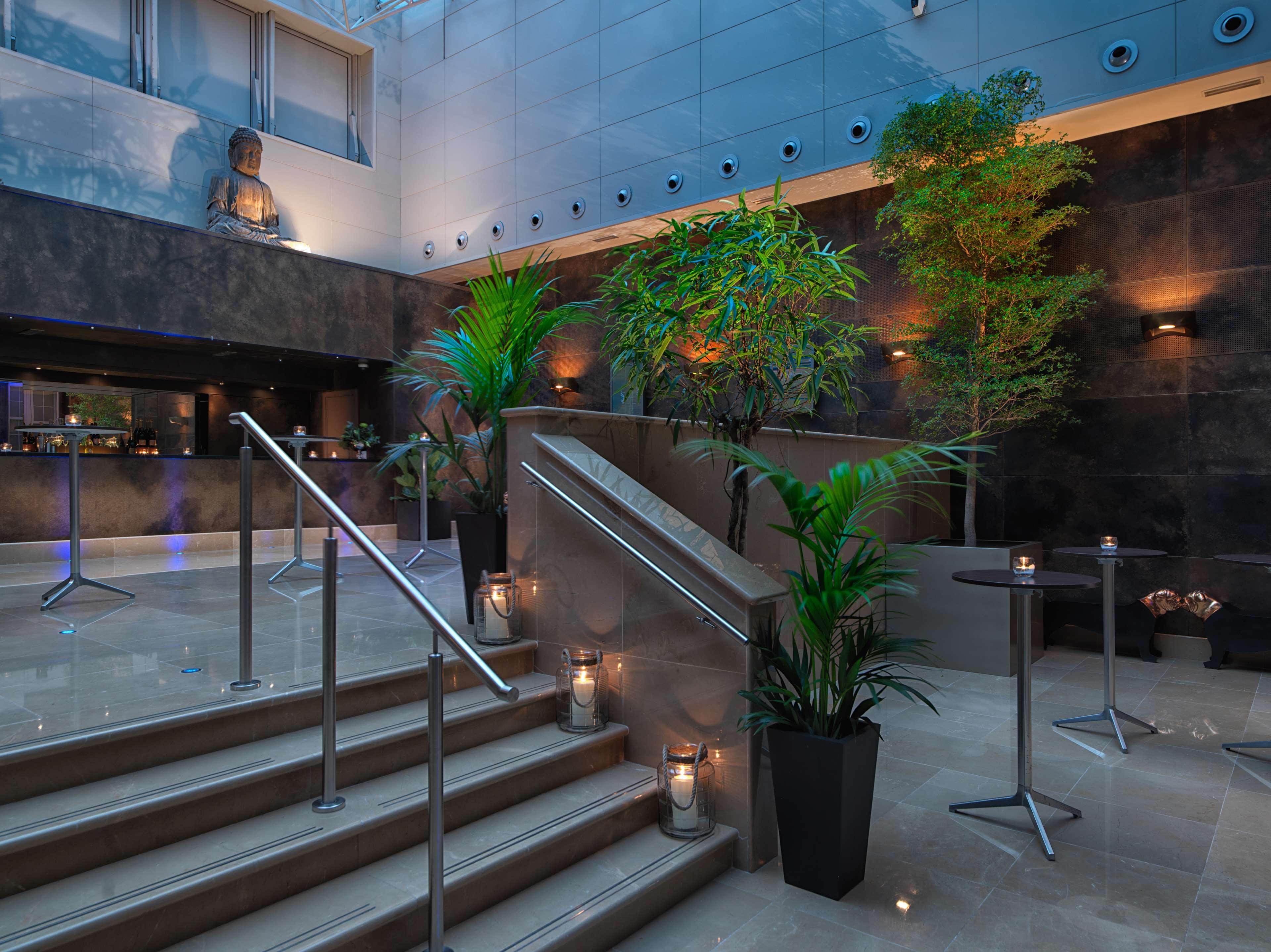 The May Fair, A Radisson Collection Hotel, Mayfair Londýn Exteriér fotografie The photo depicts a modern interior space, likely from a hotel or upscale venue. There is a stylish staircase leading upwards, flanked by decorative plants that add a touch of greenery to the environment. Soft lighting highlights the design elements,