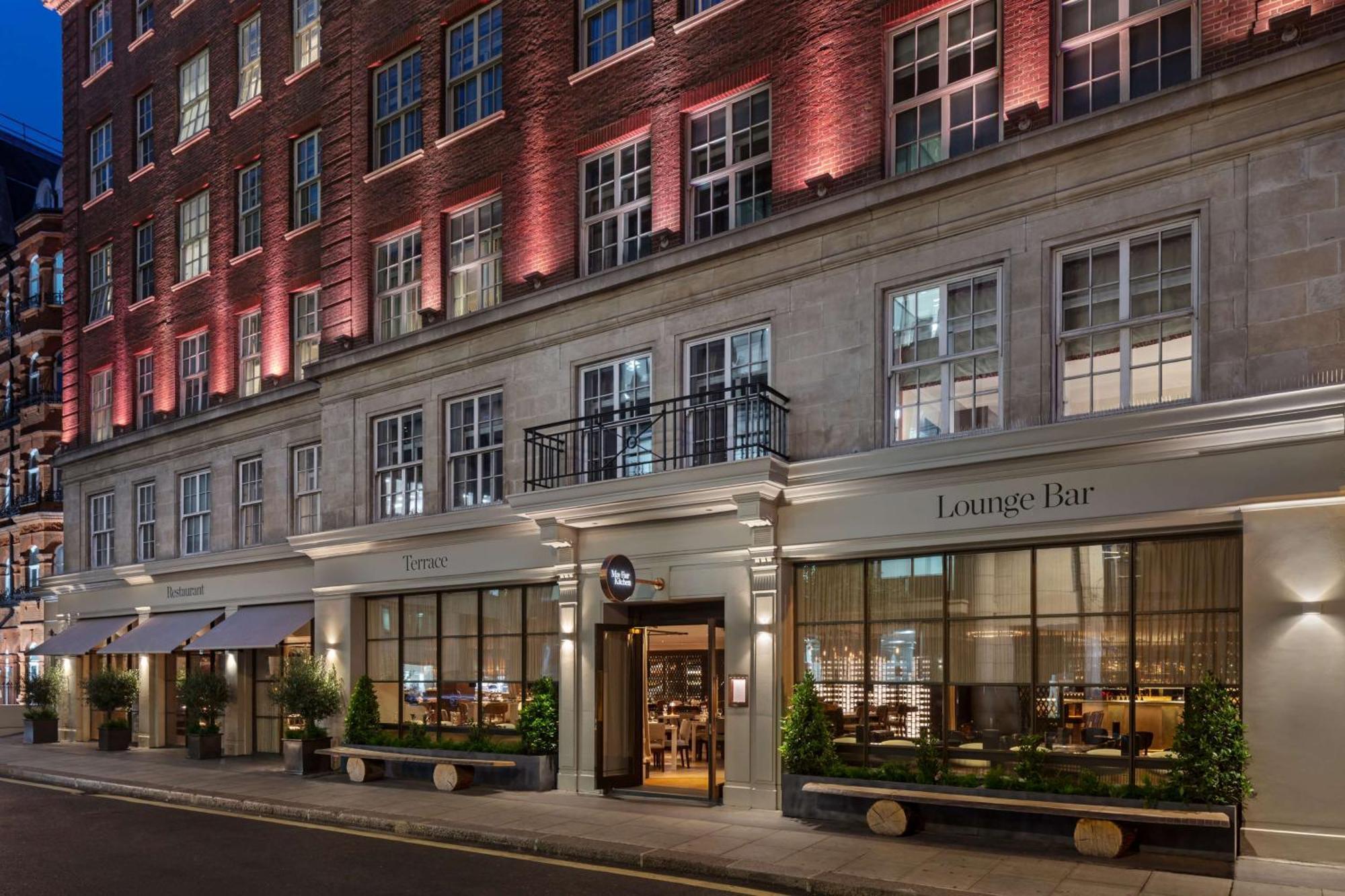 The May Fair, A Radisson Collection Hotel, Mayfair Londýn Exteriér fotografie The photo showcases a stylish building, likely a hotel or a high-end establishment. The facade features a mix of brick and stonework, and there are large windows that allow visibility into the lounge area. The entrance is marked by a sign indicating 