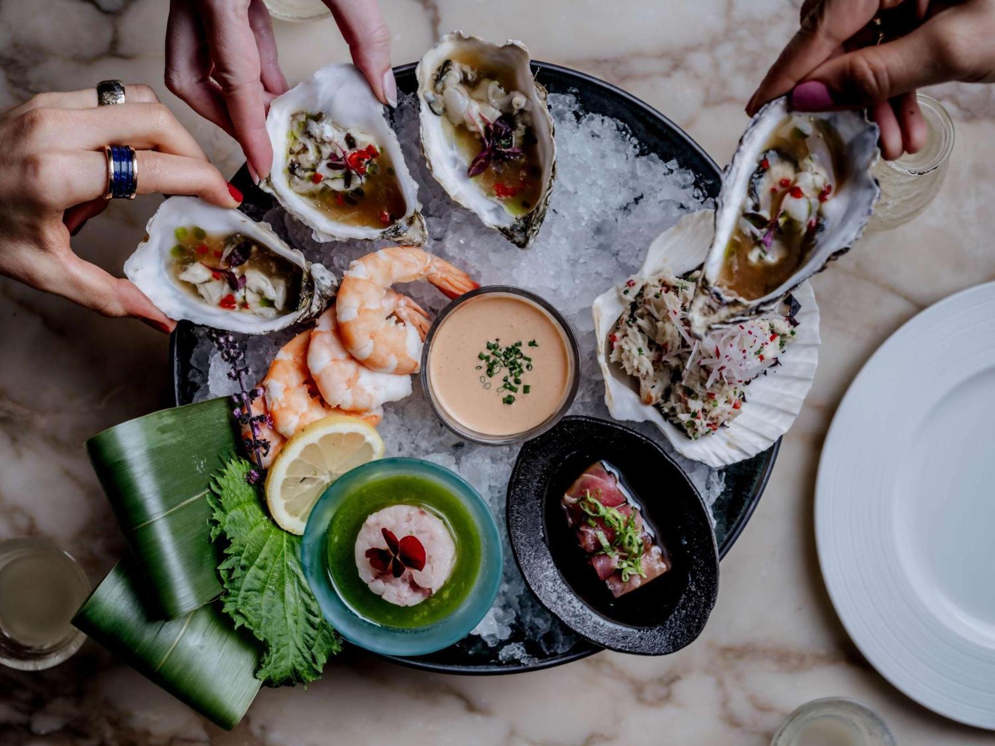The May Fair, A Radisson Collection Hotel, Mayfair Londýn Exteriér fotografie The photo displays a seafood platter arranged beautifully on a round dish filled with ice. Various types of seafood are presented, including several open oysters topped with garnishes, shrimp, and a small dish of sauce in the center. Surrounding the 