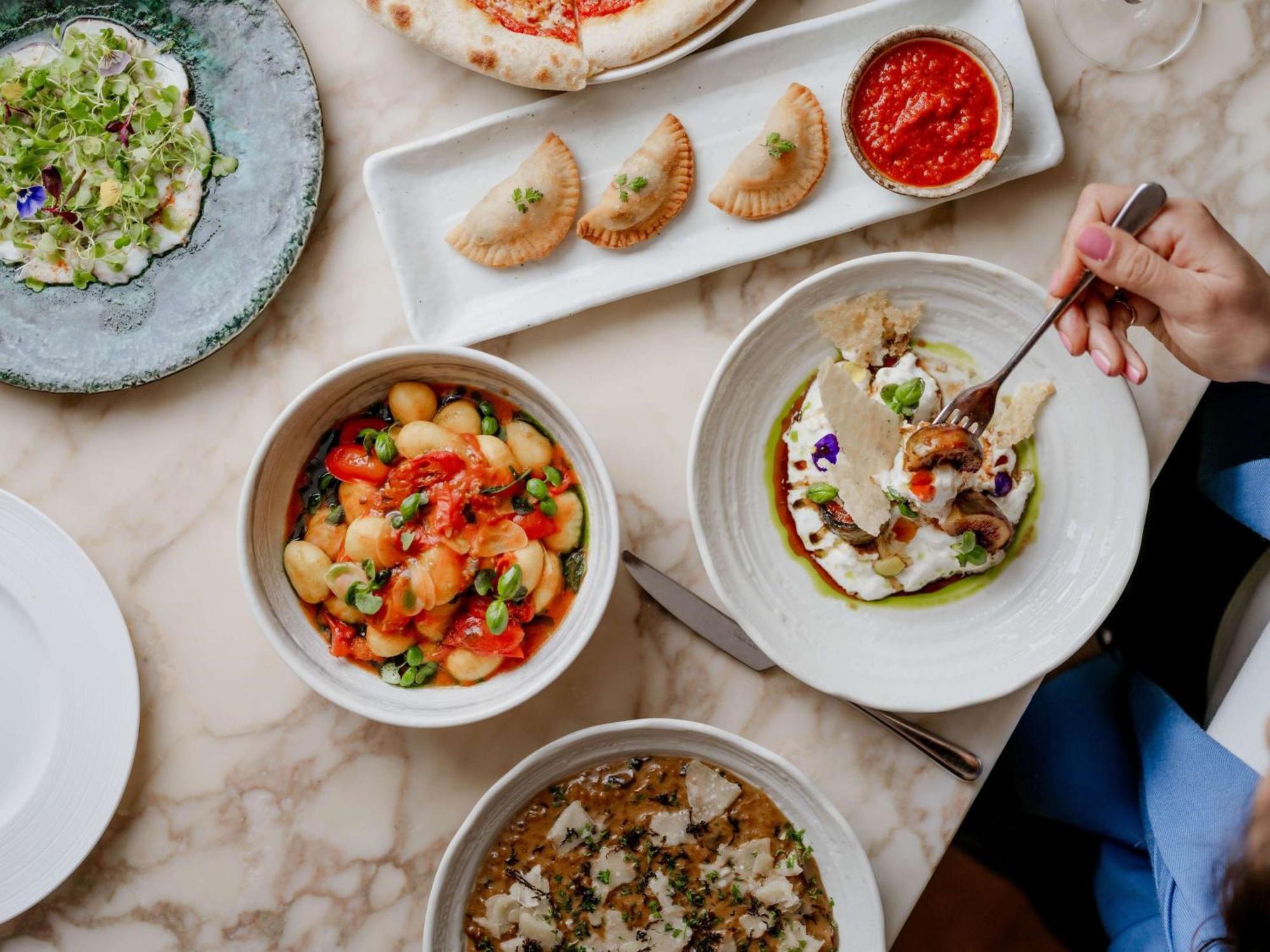 The May Fair, A Radisson Collection Hotel, Mayfair Londýn Exteriér fotografie The photo showcases a beautifully arranged table filled with various dishes. In the foreground, there are three bowls: one containing a colorful mix of gnocchi with vibrant toppings, another featuring a dish with what appears to be fish or seafood, g
